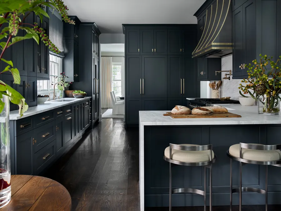 A dark navy kitchen with brass hood bands and marble counters