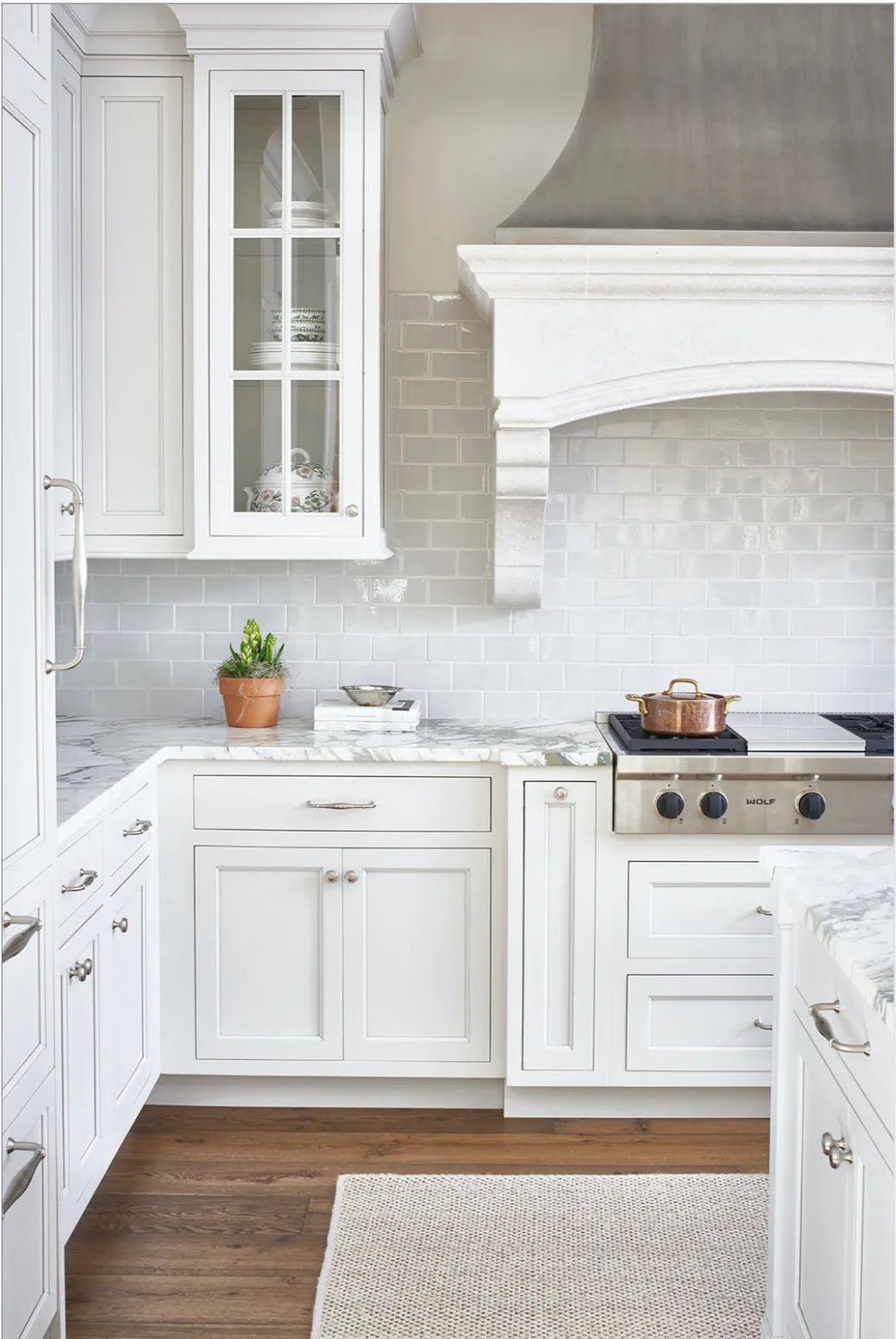 A white kitchen with a plaster hood and glass-front cabinets